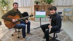 Guitar teacher and student holding their guitars during a lesson.